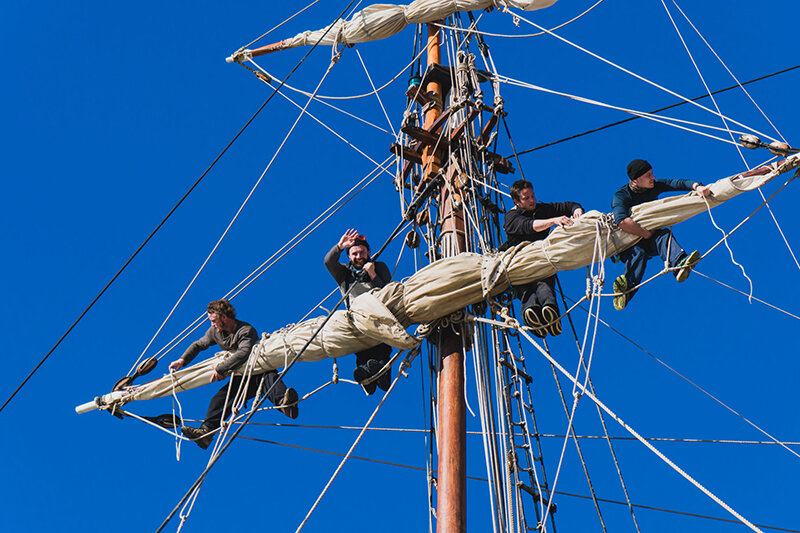 Sailors work with sails at a height on a traditional sailboat sailors work with sails at a height on a traditional sailboat in the sea